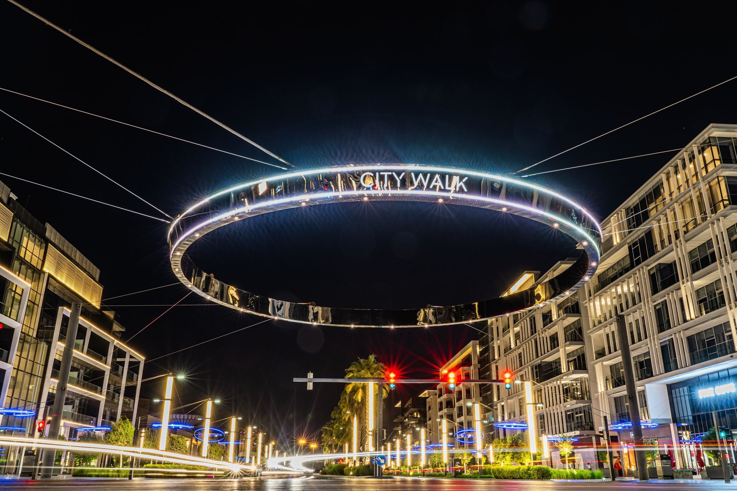 City Walk ночью: зеркальное кольцо с названием района над перекрёстком, по сторонам жилые дома с балконами