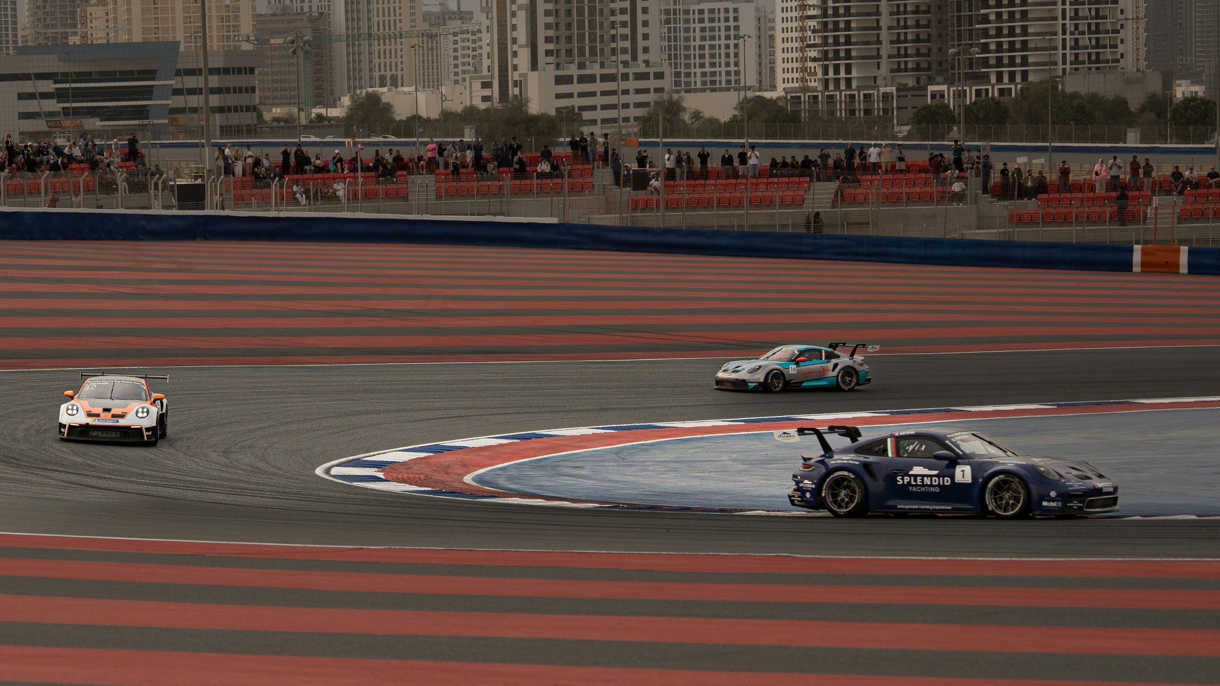 Гоночные машины на трассе Dubai Autodrome в Motor City, за трибунами жилые дома