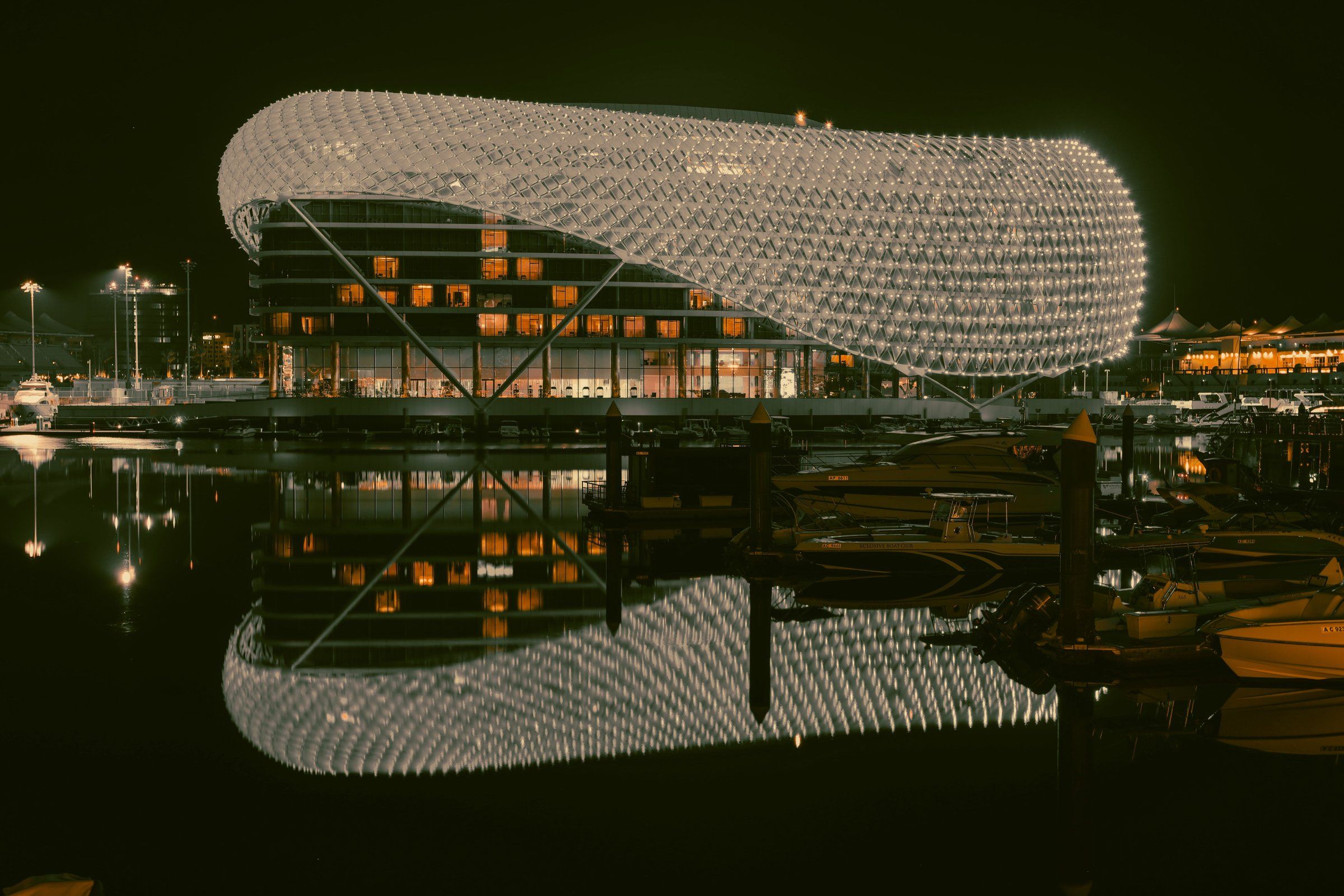 Отель W на Yas Marina ночью: светящаяся сетчатая оболочка и её отражение в воде марины, у причала катера